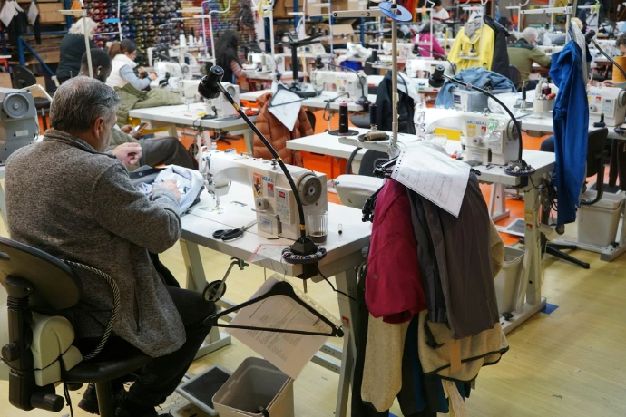 Man sewing at a machine in a busy workshop.